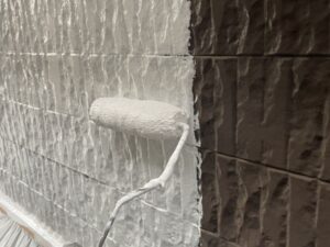 サイディング壁に白い下塗り塗料を塗っている様子