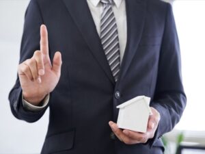 家の模型を持ち指を立てるスーツ男性